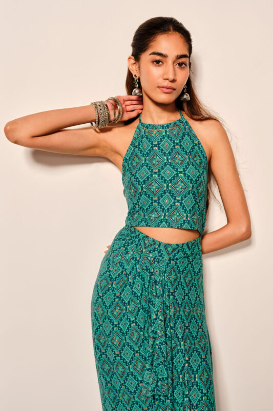 Effortless Elegance: Styling a Pink Floral blockprint dress for a Garden Day Out Woman in a sleeveless pink floral blockprint dress standing on a stone pathway surrounded by green plants and stone walls.